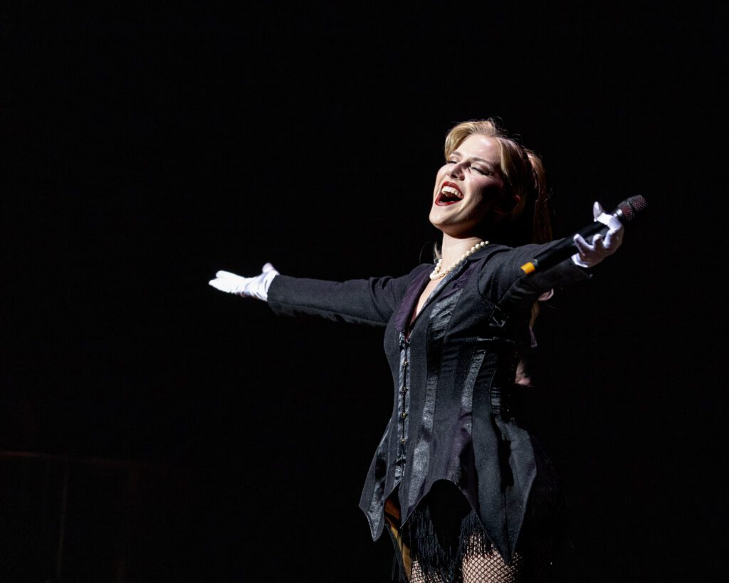 A woman sings on stage, arms open wide to the crowd