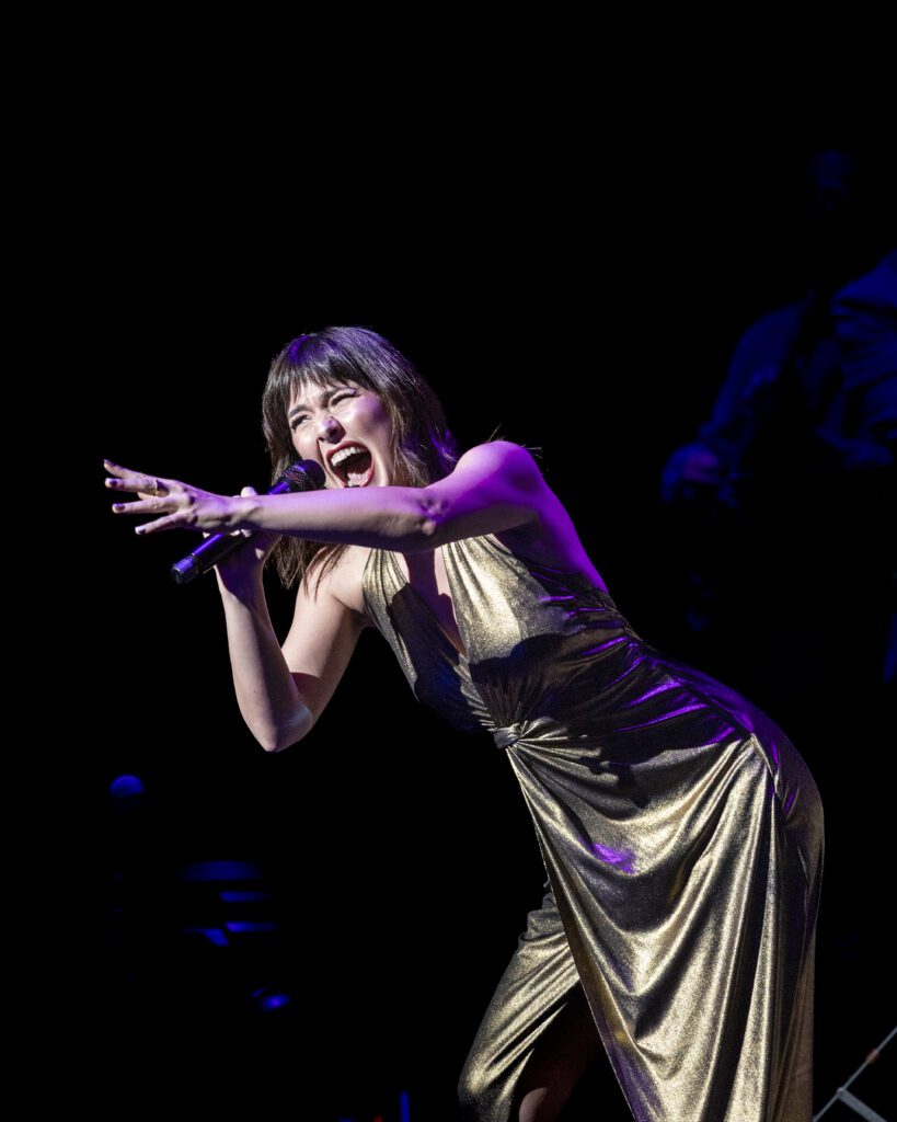 A woman sings powerfully on stage and reaches for the crowd